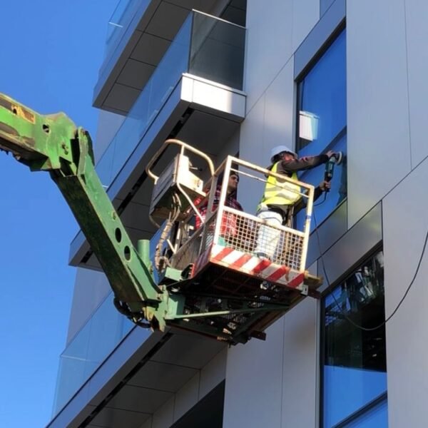 Techniker im Hubarbeitskorb poliert eine Fassadenverglasung von außen – professionelle Glasaufbereitung in großer Höhe